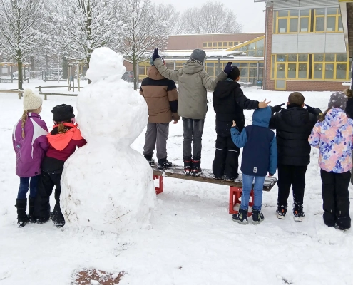 Kinder auf dem Schulhof mit Schneemann