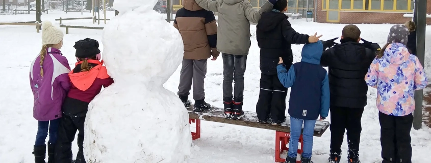 Kinder auf dem Schulhof mit Schneemann